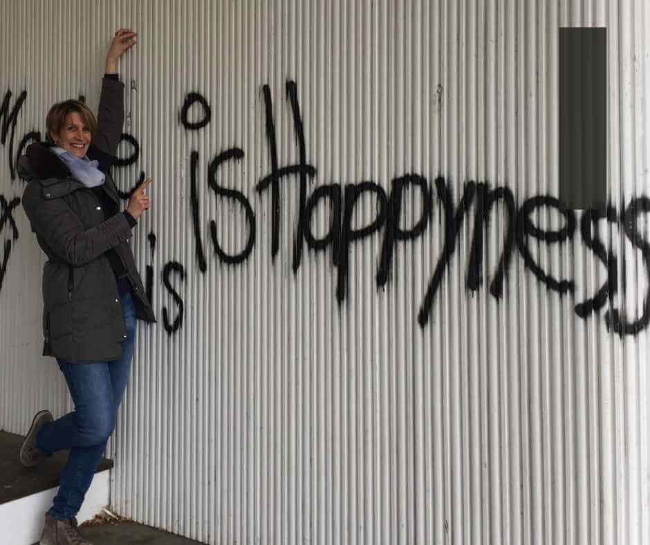 Frau vor einer Wellblechwand auf der "is Happiness" steht